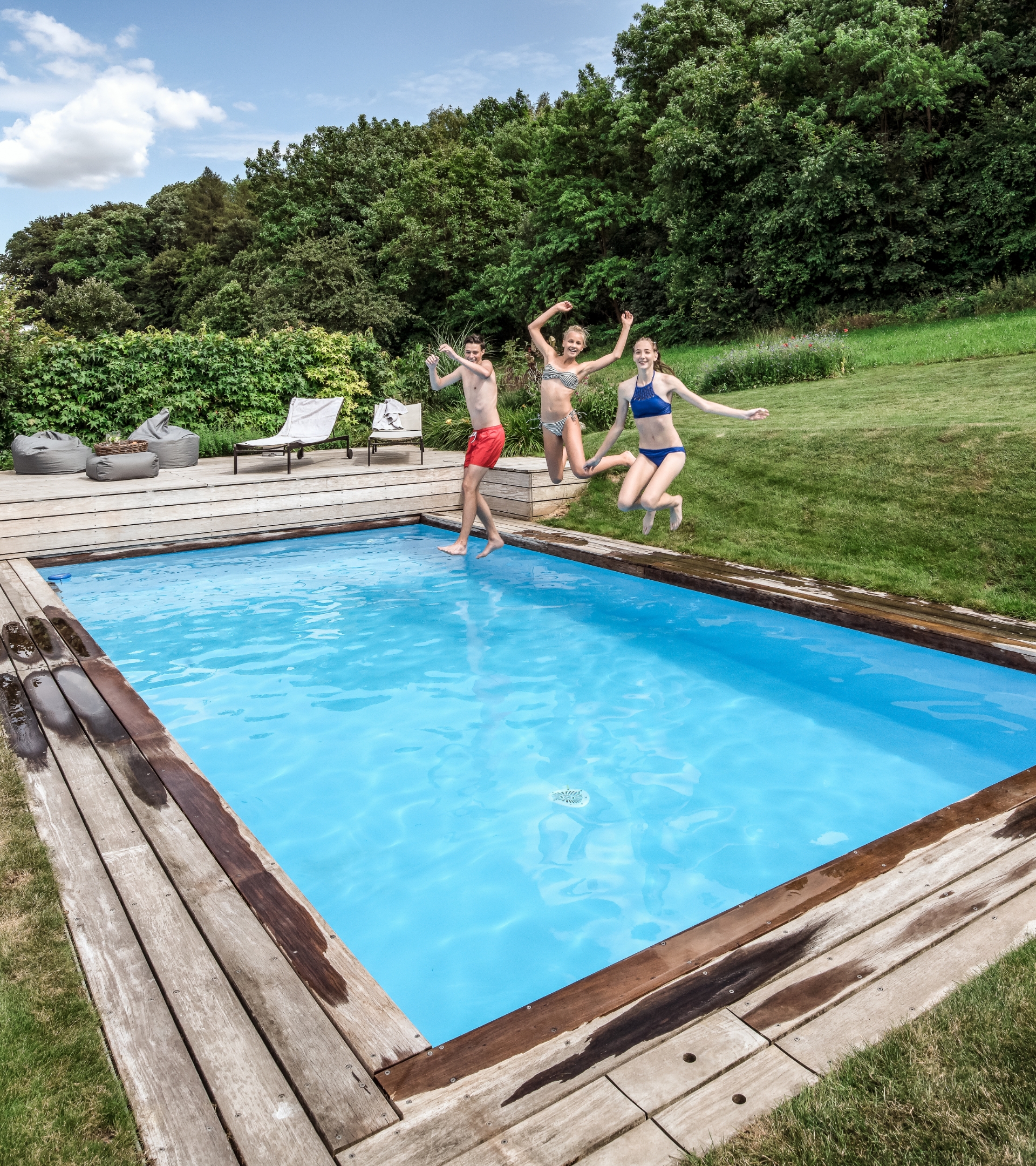 Drei junge Personen hüpfen vergnügt in einen Pool in einem Garten